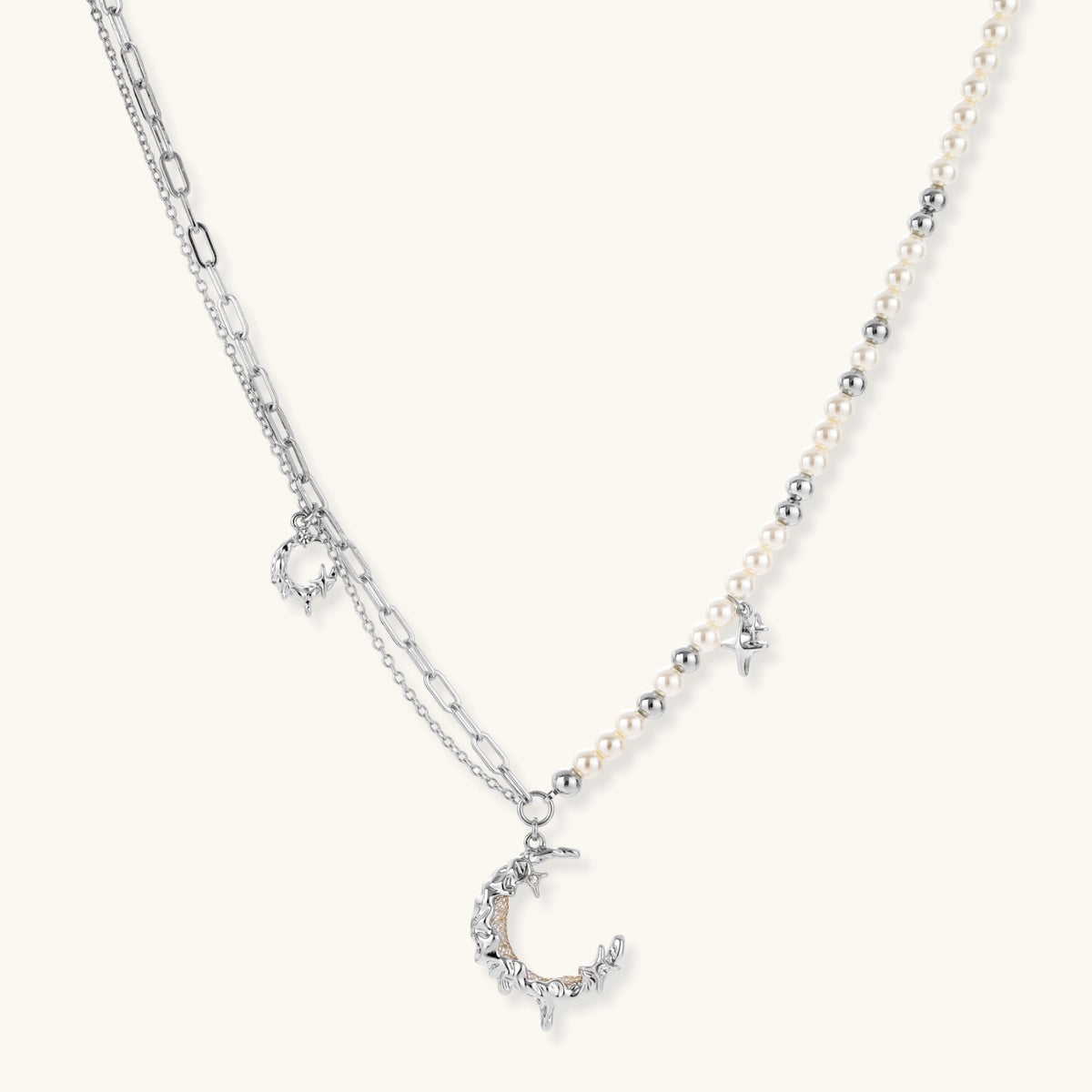 Silver-toned crescent moon pendant with star accents on pearl and chain necklace against white background.