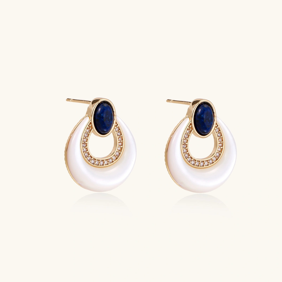 Gold plated stud earrings with an oval lapis lazuli top, CZ-lined teardrop loop and white MOP crescent on a cream background.
