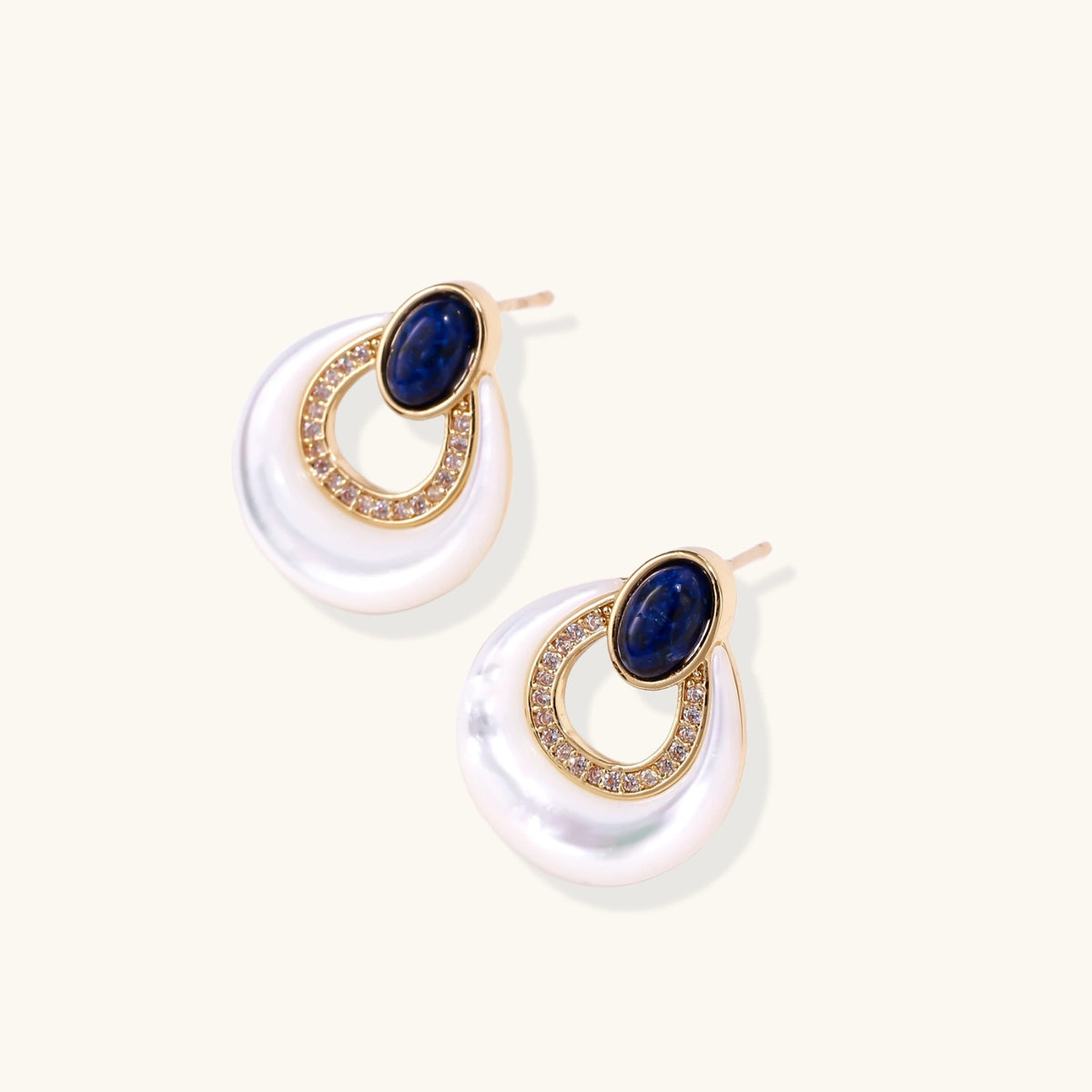 Gold plated stud earrings with an oval lapis lazuli top, CZ-lined teardrop loop and white MOP crescent on a cream background.
