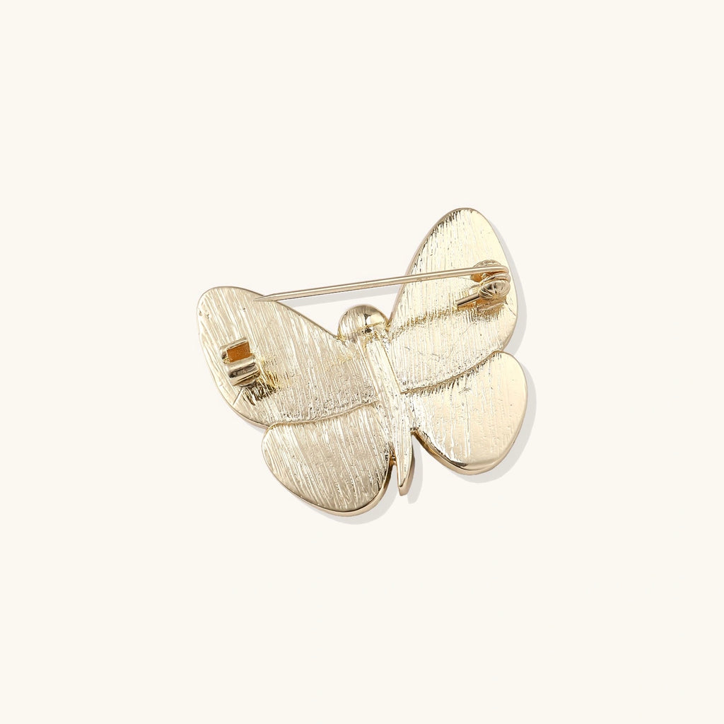 Gold-plated butterfly brooch with iridescent abalone shell wings and freshwater pearl accent on cream background.