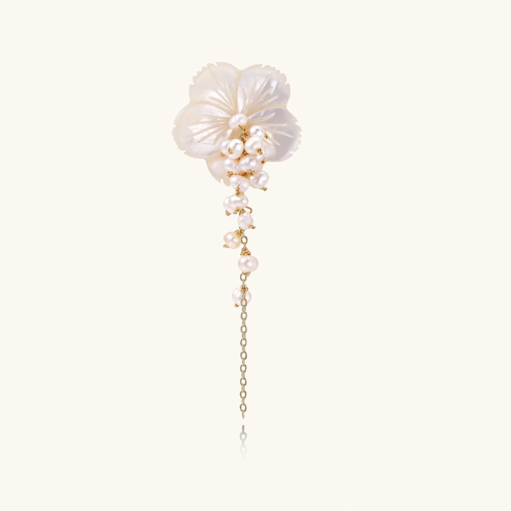 Iridescent shell flower brooch with carved petals and cascading freshwater pearls on gold chain against cream background.