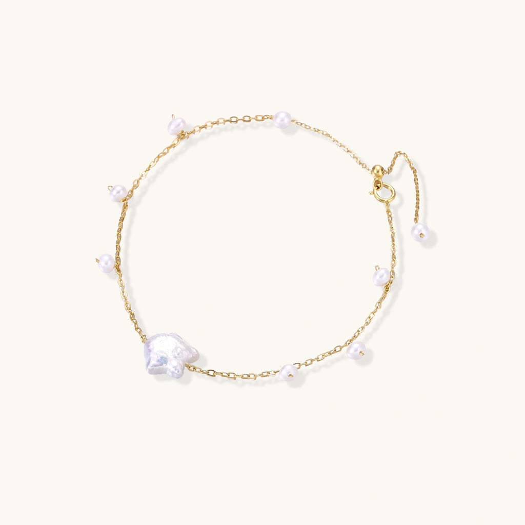 Delicate gold chain bracelet with baroque pearl centerpiece and small freshwater pearls on cream background.