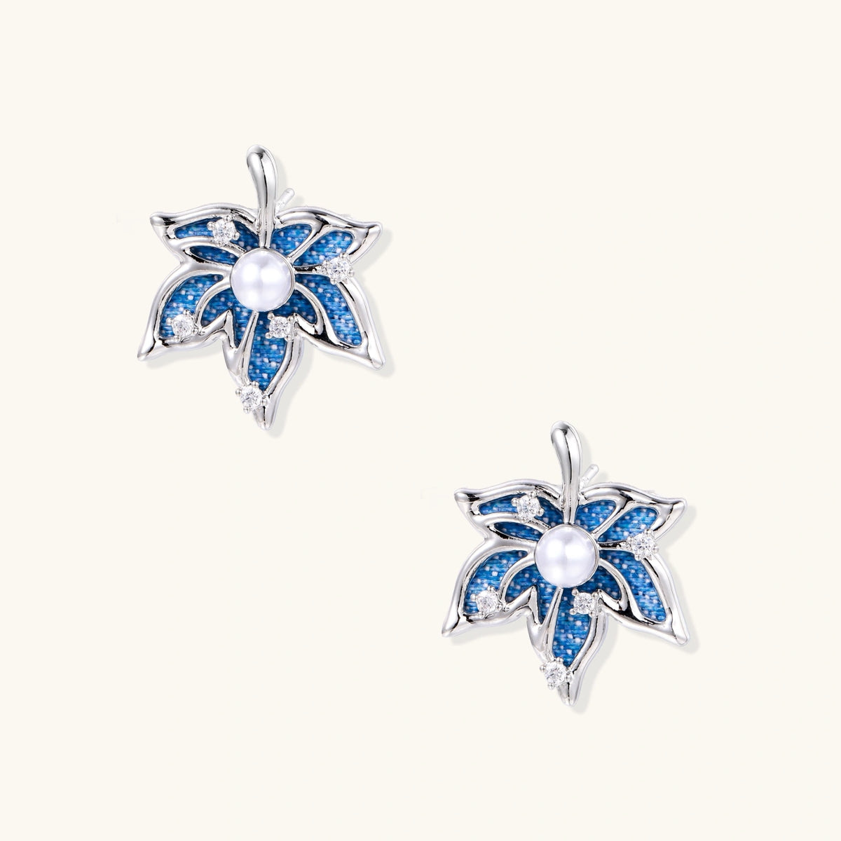Pair of maple leaf stud earrings with blue denim fabric, a white bead center and zirconia accents in white gold plated eco-brass.