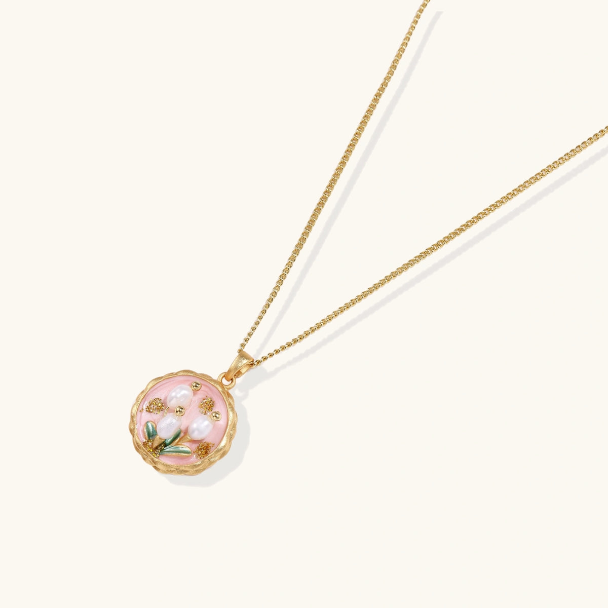 Gold pendant with pink enamel backdrop, white freshwater pearls as tulip blooms, and green leaf accents on rope chain.