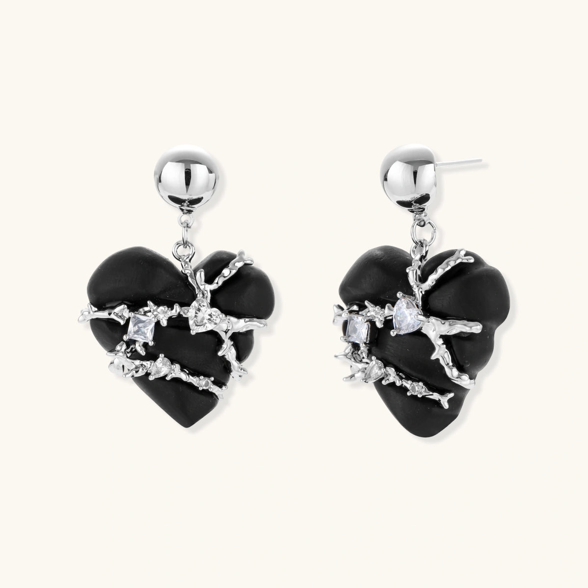 Pair of black heart drop earrings in ebony wood with silver-tone thorny vines, zirconia stones and round ball studs on cream background.