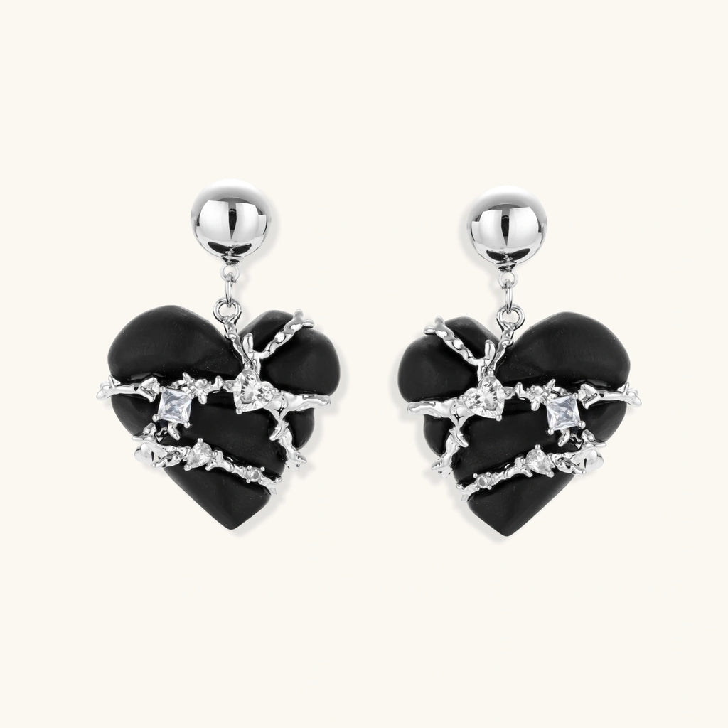 Pair of black heart drop earrings in ebony wood with silver-tone thorny vines, zirconia stones and round ball studs on cream background.