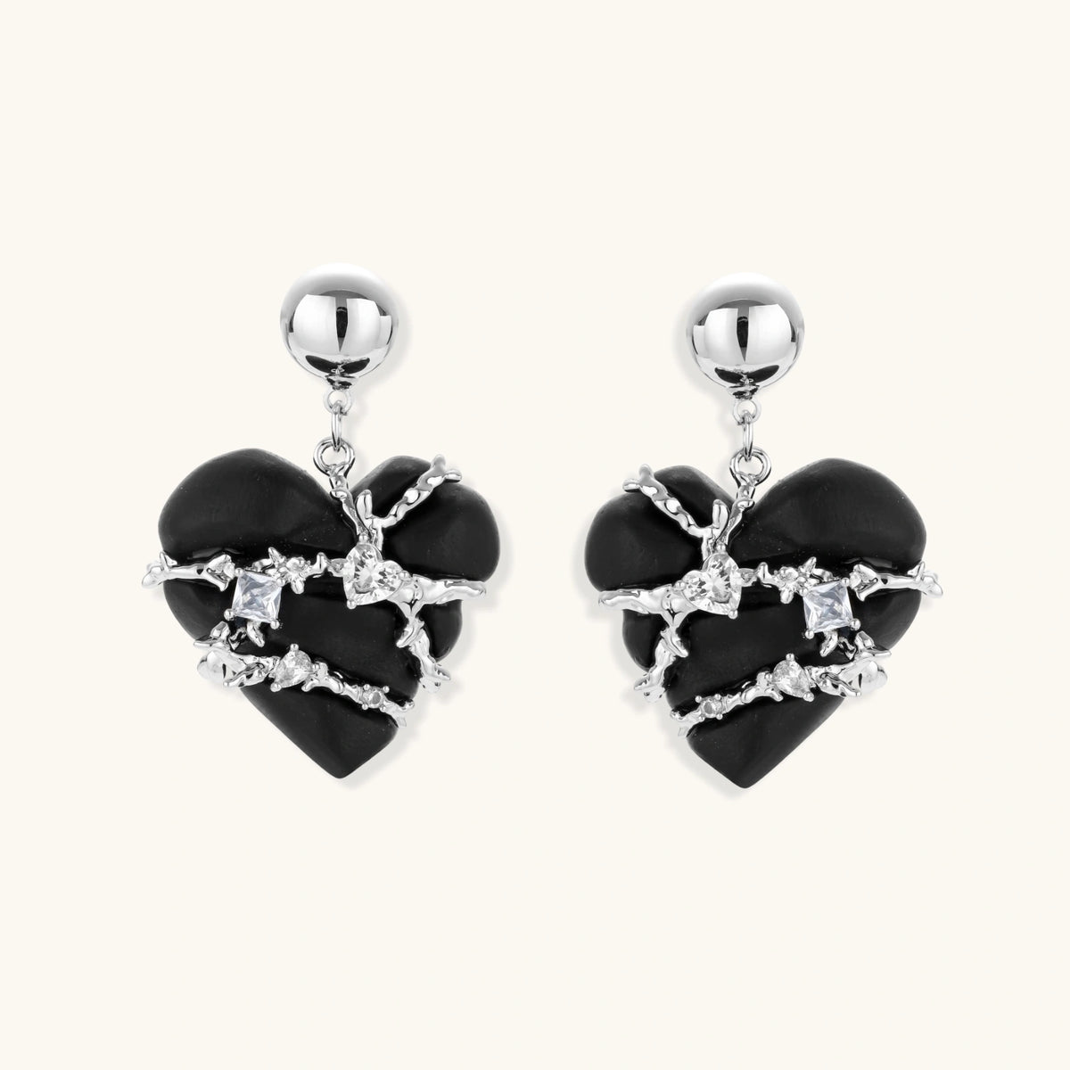 Pair of black heart drop earrings in ebony wood with silver-tone thorny vines, zirconia stones and round ball studs on cream background.