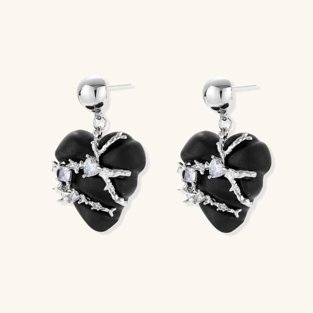 Pair of black heart drop earrings in ebony wood with silver-tone thorny vines, zirconia stones and round ball studs on cream background.