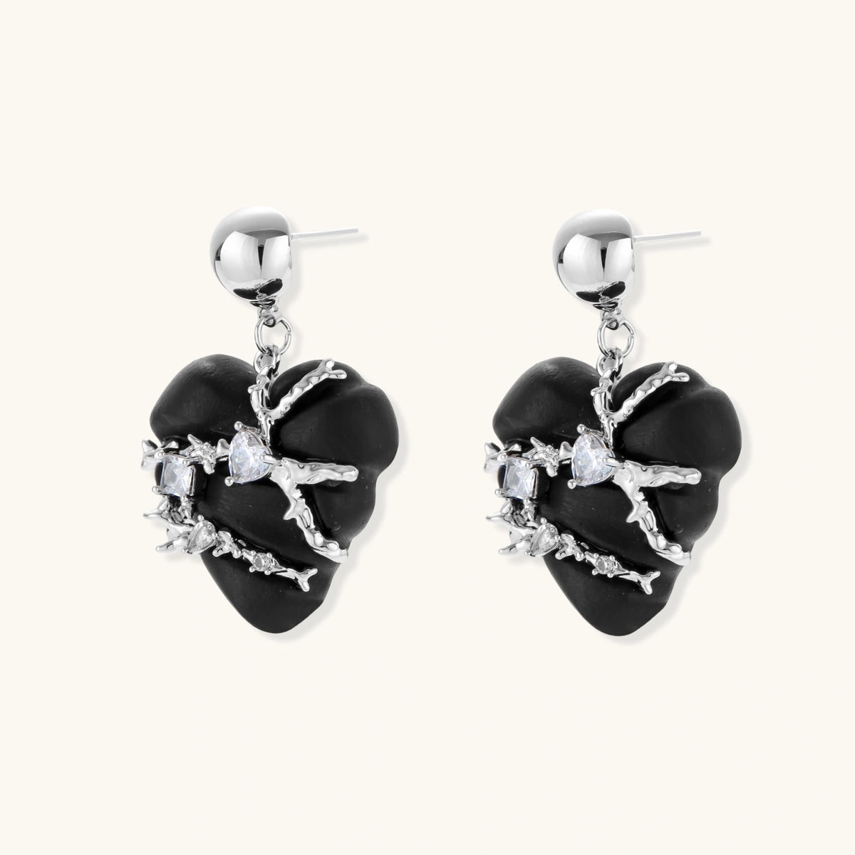 Pair of black heart drop earrings in ebony wood with silver-tone thorny vines, zirconia stones and round ball studs on cream background.