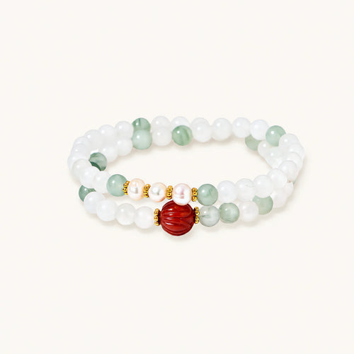 Three layered white beaded bracelets with carved orange agate lotus centerpiece and freshwater pearls on cream background.