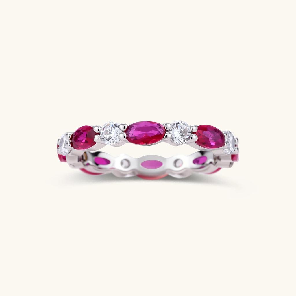 Front view of a white gold plated eco-brass eternity band with alternating red ruby crystal ovals and round clear stones.