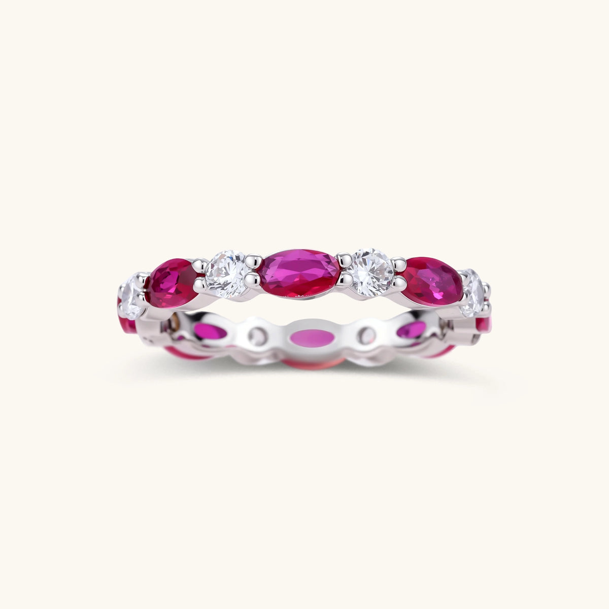Front view of a white gold plated eco-brass eternity band with alternating red ruby crystal ovals and round clear stones.