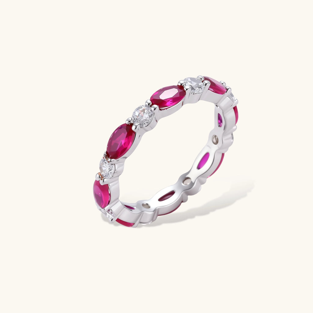 Front view of a white gold plated eco-brass eternity band with alternating red ruby crystal ovals and round clear stones.